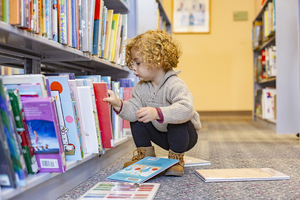 Curly Haired Child Selecting Books From A Shelf In 2025 04 03 08 01 57 Utc Klein